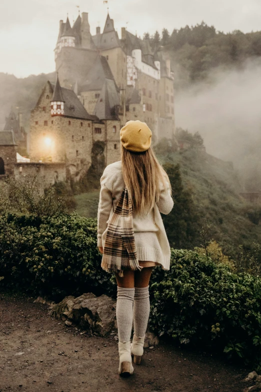 a woman standing in front of a castle on a foggy day, traveling through the mountains, looking cute, thighs, trending photo