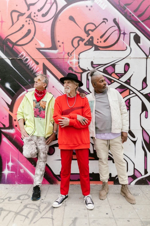 a group of people standing in front of a graffiti wall, a portrait, inspired by Edwin Georgi, graffiti, george clinton, promotional image, 3 - piece, reds