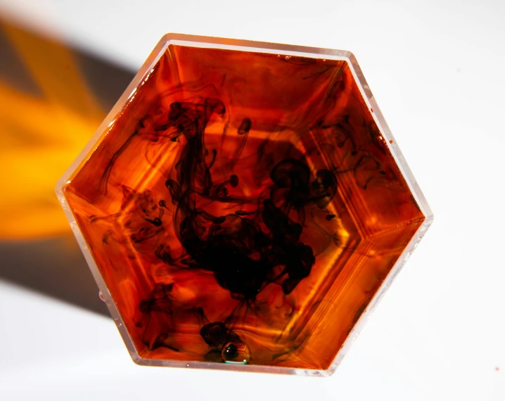 a close up of a glass object on a table, a microscopic photo, inspired by Michelangelo Unterberger, pexels, crimson - black beehive, amber, top angle view, hexagonal shaped