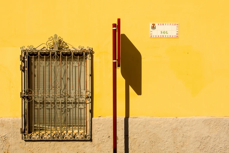 a street sign in front of a yellow building, inspired by Josep Rovira Soler, pexels contest winner, perfect shadows, colorful with red hues, an intricate, a small