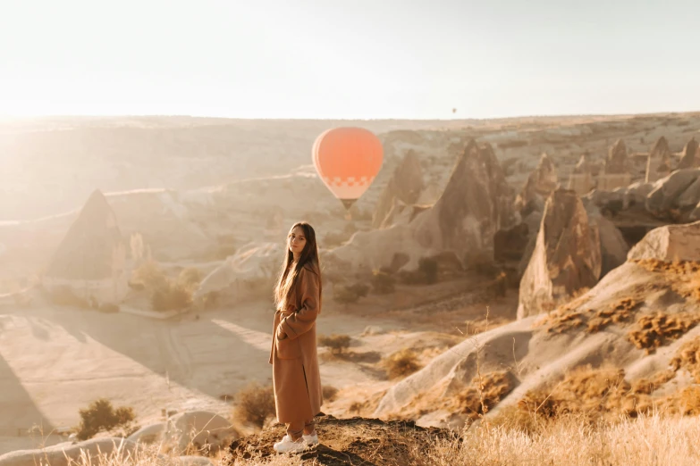 a woman standing on top of a hill holding a red balloon, by irakli nadar, pexels contest winner, looking off to the side, brown, hot air balloon, avatar image