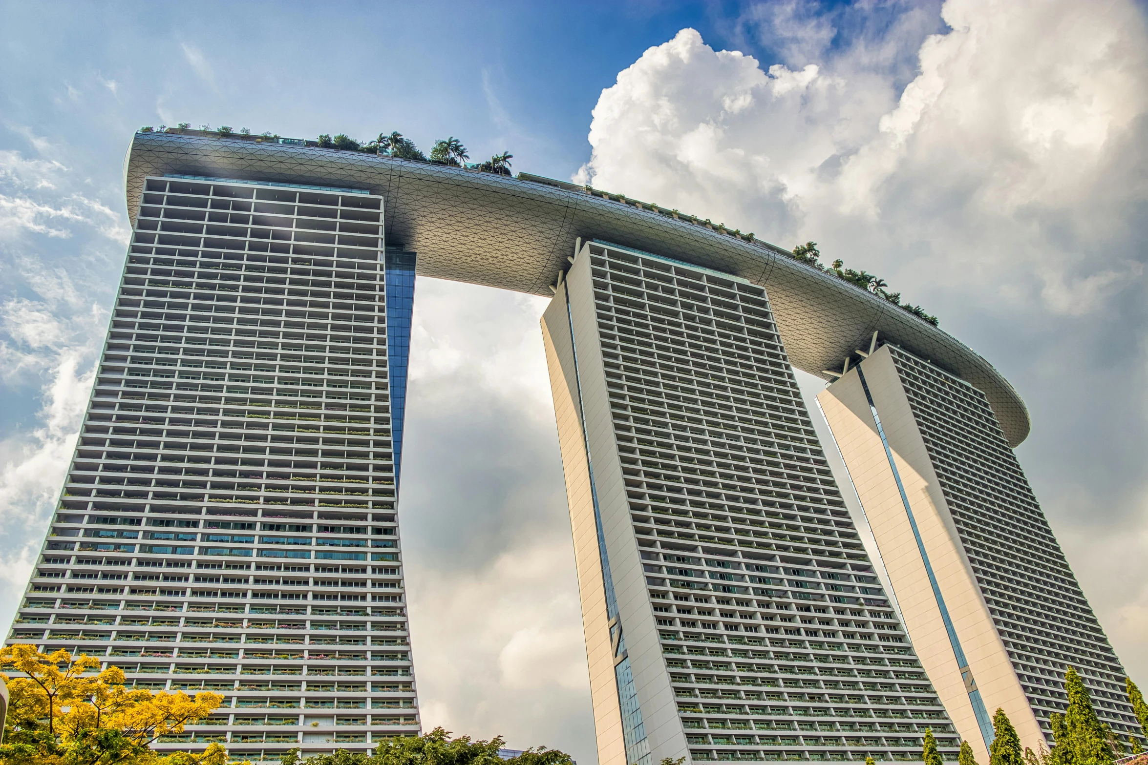 a couple of tall buildings sitting on top of a lush green field, inspired by Zha Shibiao, pexels contest winner, singapore esplanade, white sweeping arches, viewed from the ground, viewed from the ocean