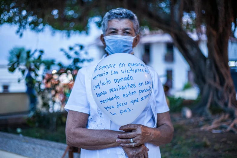 a man wearing a face mask holding a balloon, by Juan Giménez, with some hand written letters, elderly woman, puerto rico, wearing white cloths