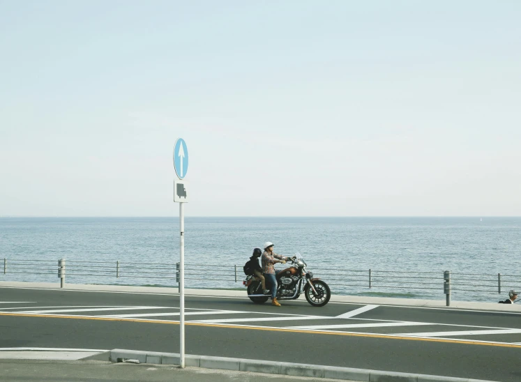 a couple of people riding on the back of a motorcycle, unsplash, shin hanga, summer street near a beach, b - roll, seaview, street corner