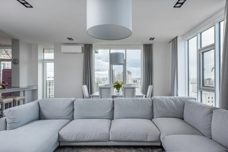 a living room filled with furniture and a large window, by Adam Marczyński, unsplash contest winner, light and space, white l shaped couch, grey and silver, luxury condo interior, led lighting