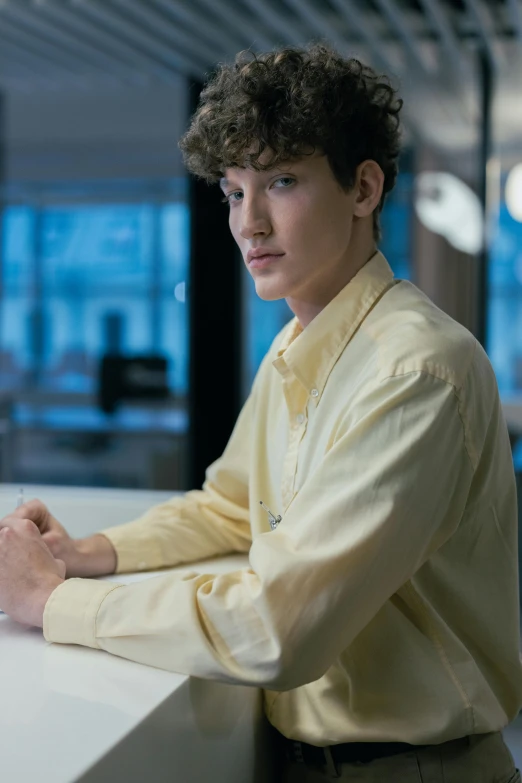 a young man sitting at a desk in an office, an album cover, inspired by John Luke, unsplash, renaissance, office clothes, attractive androgynous humanoid, gold shirt, photographed for reuters