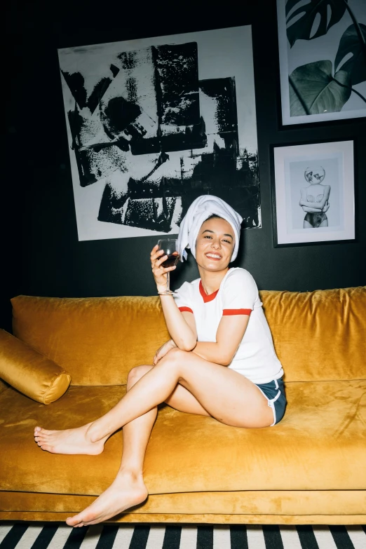 a woman sitting on a couch holding a cell phone, a polaroid photo, bra and shorts streetwear, wearing a baseball hat, at the sitting couch, emilia clarke