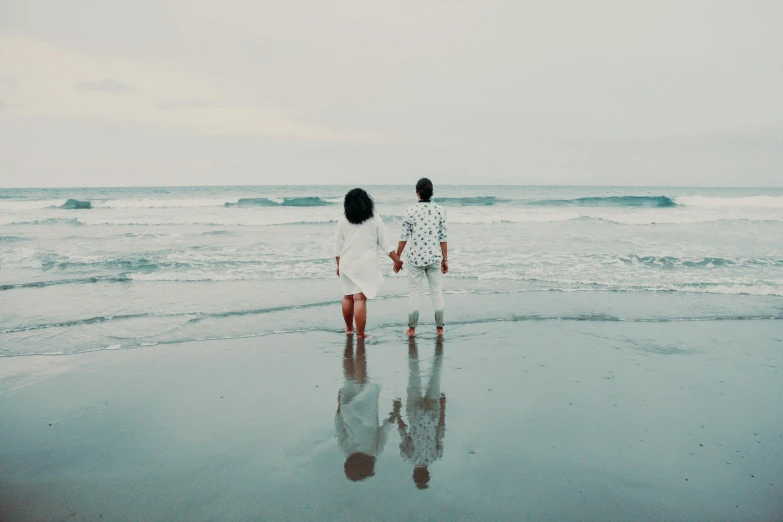 a couple of people standing on top of a beach, pexels contest winner, minimalism, wet feet in water, looking off into the distance, very romantic, white hue