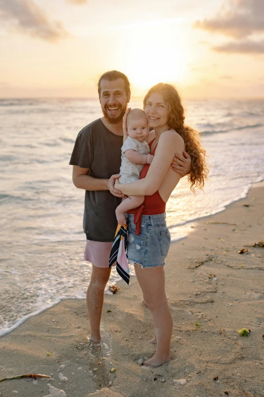 a man and woman holding a baby on a beach, sun down, portrait photo of a backdrop, standing straight, avatar image