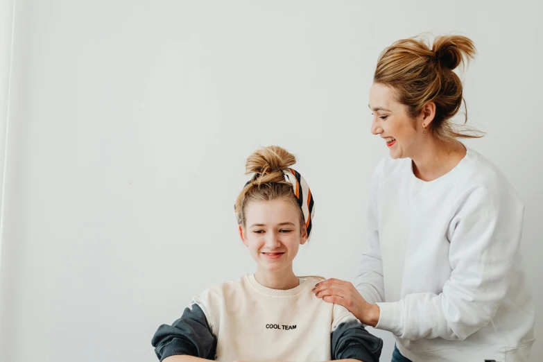 a woman helping a young girl with her hair, by Emma Andijewska, trending on pexels, wearing a shirt, spa, plain background, straya