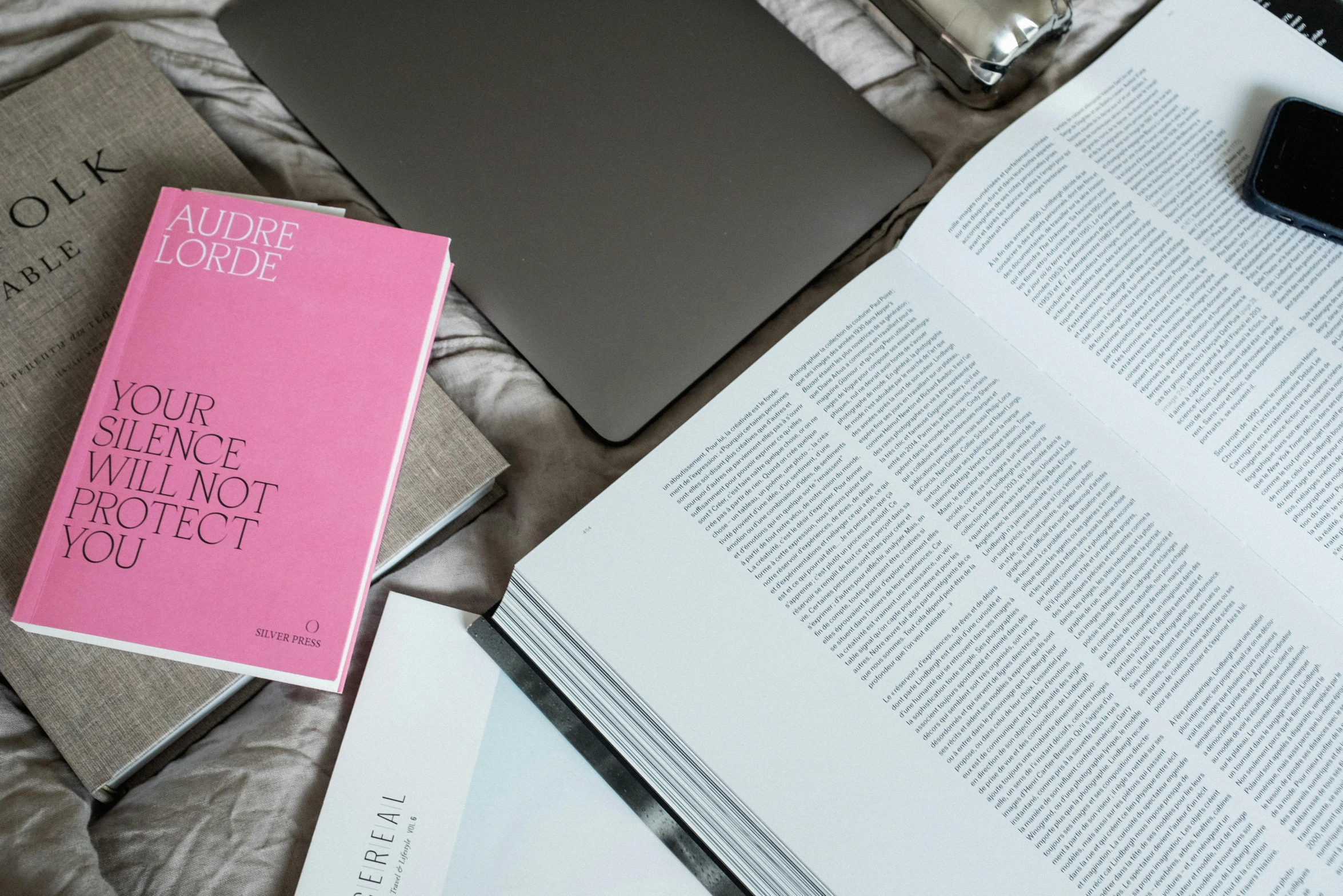 a book sitting on top of a bed next to a laptop, a still life, unsplash, academic art, white and pink, vogue journal cover, detail shot, magenta and gray