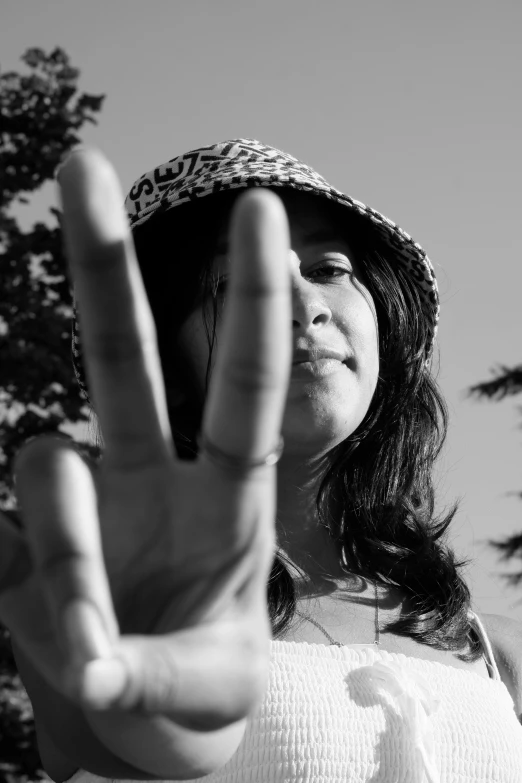 a woman making a peace sign with her hand, a black and white photo, by Altichiero, wearing a hat, low angle!!!!, ((portrait)), 4 2 0