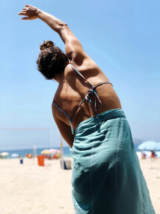 a woman standing on top of a sandy beach, wearing a towel, his back is turned, armpit, profile pic