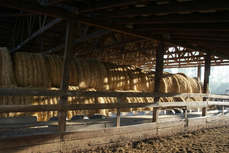 a barn filled with lots of hay next to a wooden fence, feed troughs, sun shaft, lachlan bailey, indoor picture