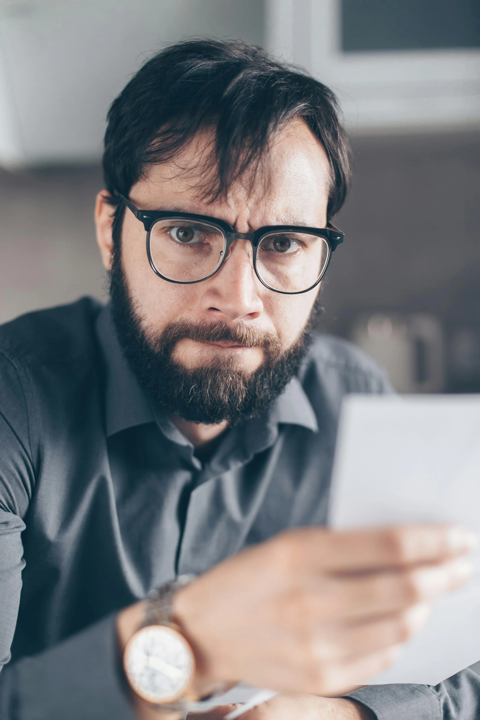 a man sitting at a table looking at a piece of paper, trending on reddit, looking angry, in square-rimmed glasses, looking at his phone, unkempt beard