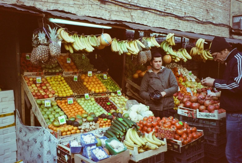 a man standing in front of a fruit stand, a colorized photo, inspired by Vivian Maier, unsplash, qajar art, 🦩🪐🐞👩🏻🦳, 70s photo, album photo, shot on expired instamatic film