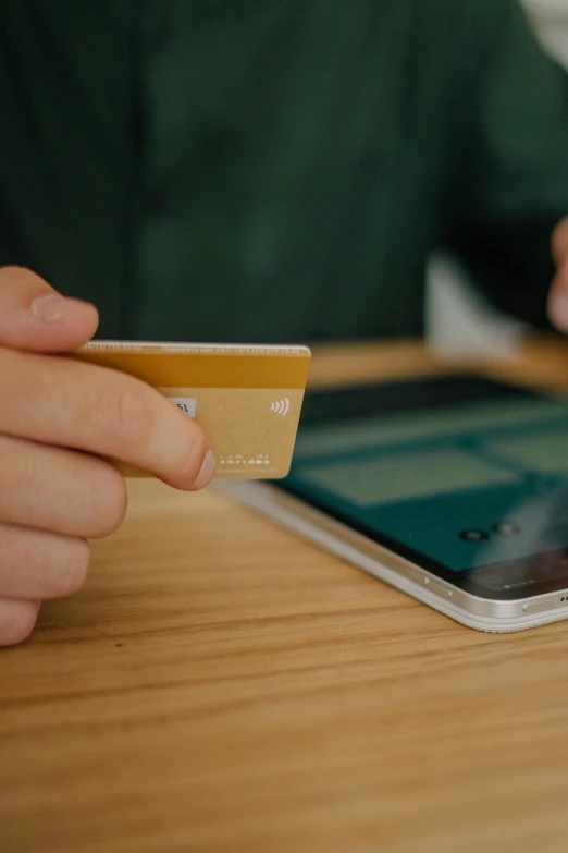 a person holding a credit card while sitting at a table, by Carey Morris, mobile learning app prototype, paul barson, controversial, at checkout