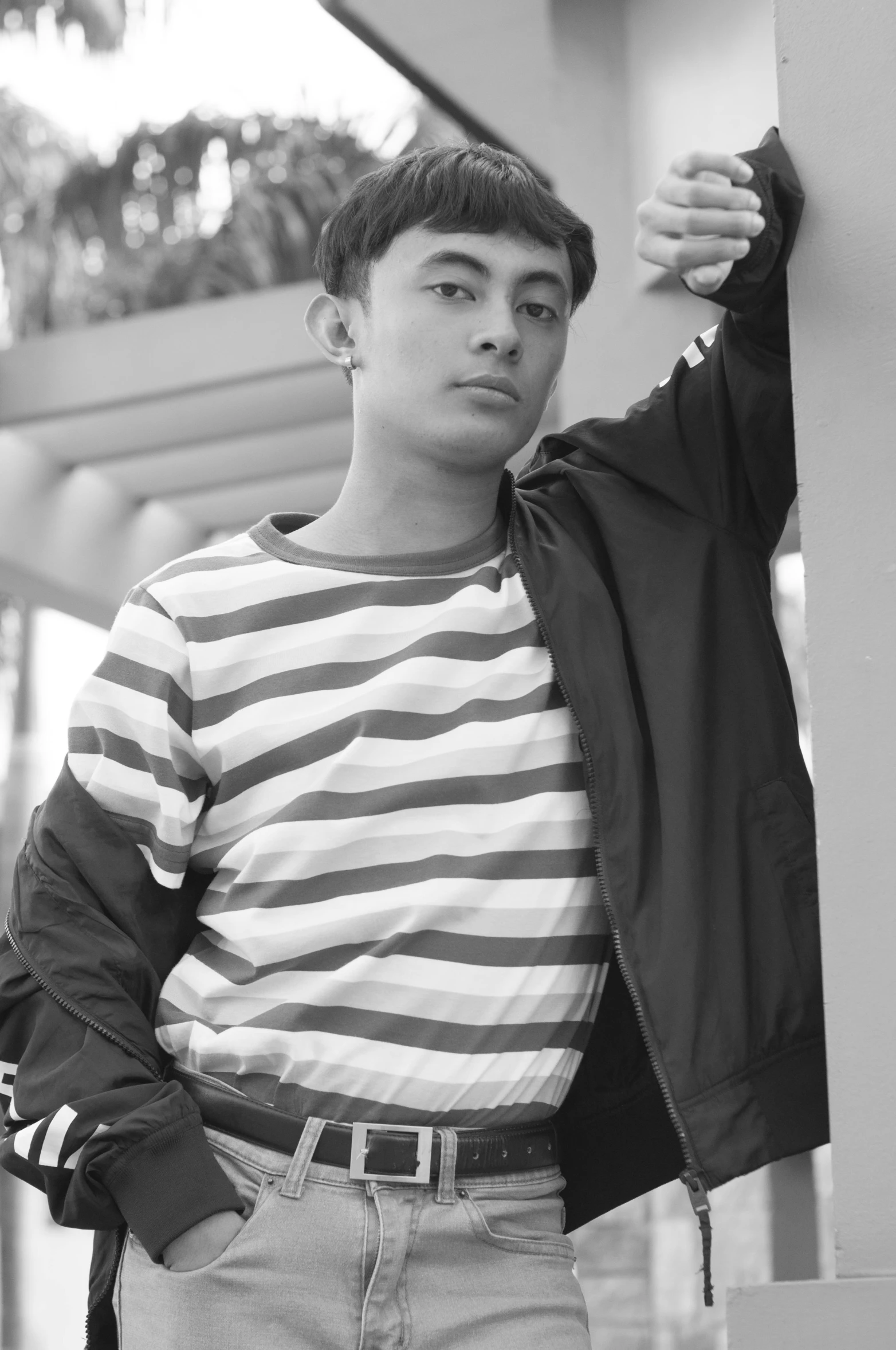 a black and white photo of a man leaning against a wall, inspired by Adam Dario Keel, wearing stripe shirt, around 1 9 years old, south east asian with round face, at a mall