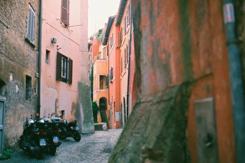 a couple of motorcycles parked on the side of a street, by Emma Andijewska, unsplash contest winner, renaissance, orange pastel colors, old village, photo taken on fujifilm superia, all roads lead to rome