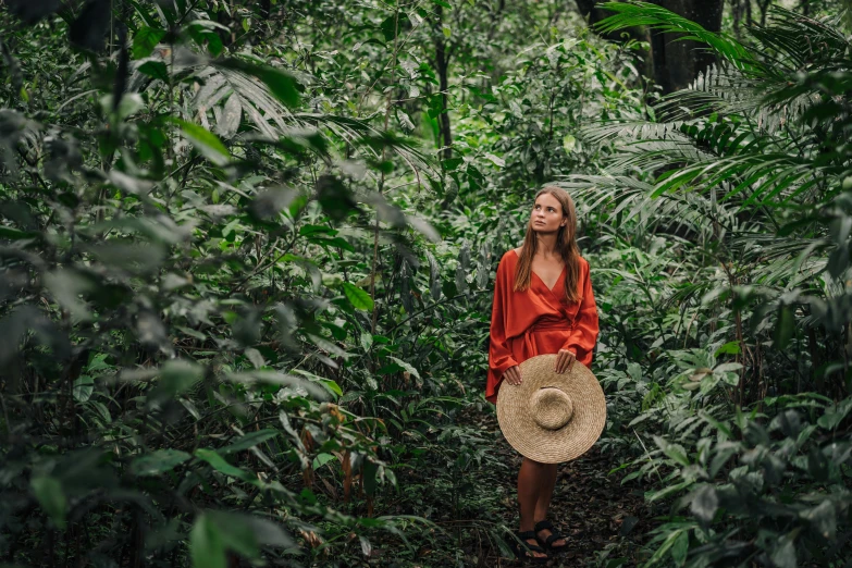 a woman standing in the middle of a forest, by Emma Andijewska, sumatraism, orange jumpsuit, wearing a travel hat, avatar image, conde nast traveler photo