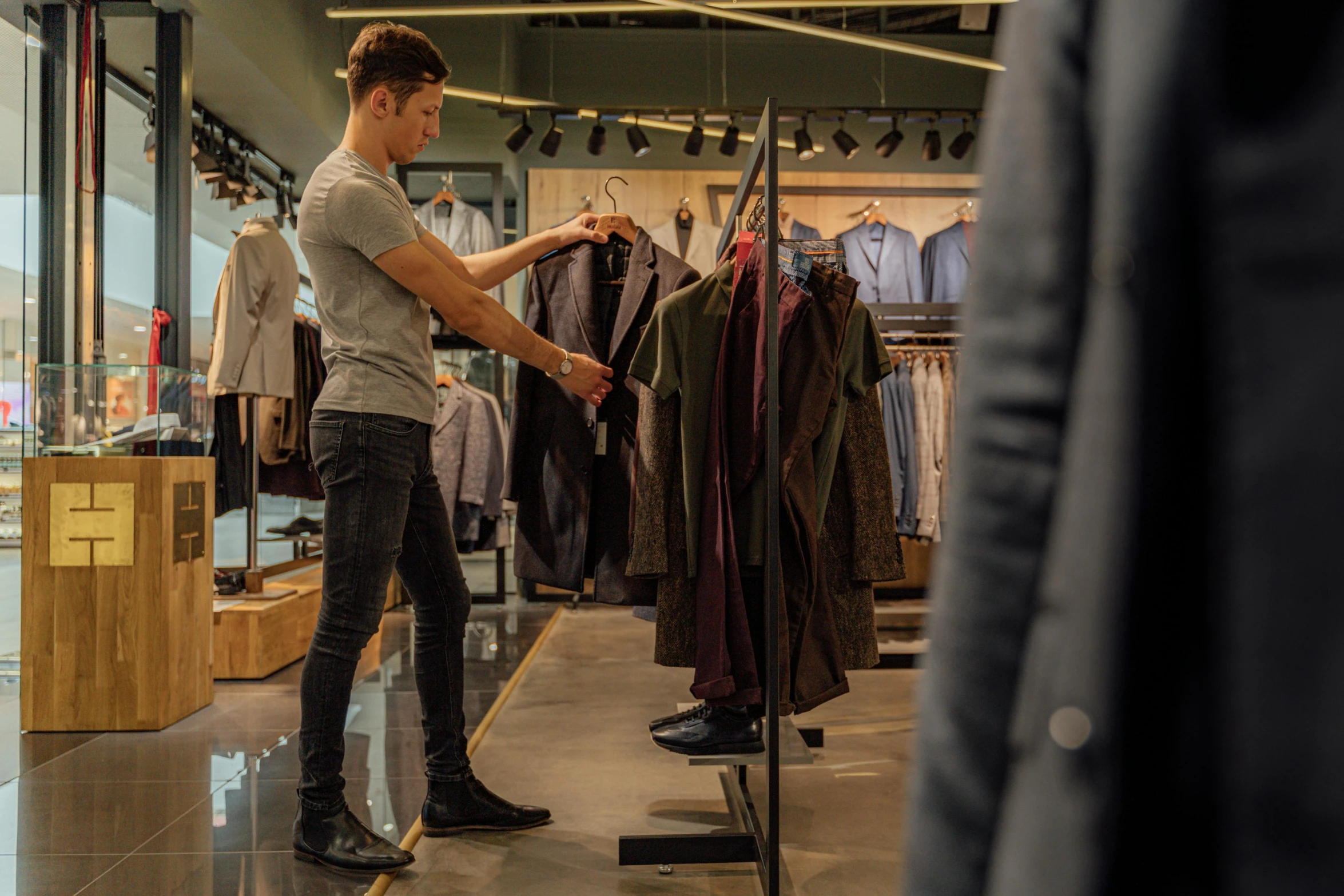 a man standing in front of a rack of clothes, with a sleek spoiler, people shopping, in style of kyrill kotashev, tall angle