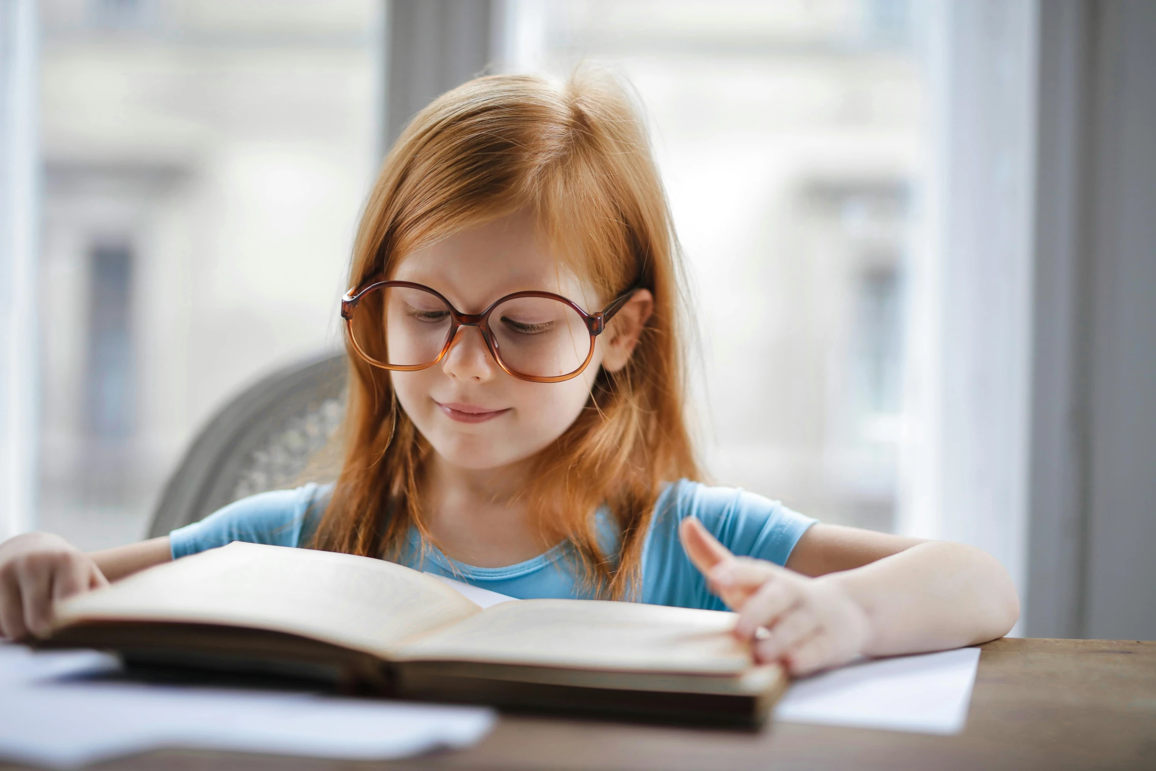 a little girl sitting at a table reading a book, pexels contest winner, square rimmed glasses, school curriculum expert, looking across the shoulder, thumbnail
