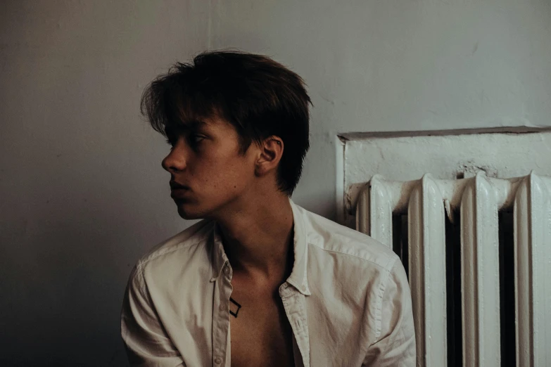 a shirtless man sitting in front of a radiator, an album cover, inspired by Nikolaj Abraham Abildgaard, pexels contest winner, detailed face of a asian boy, wearing a white button up shirt, side profile view, androgynous person