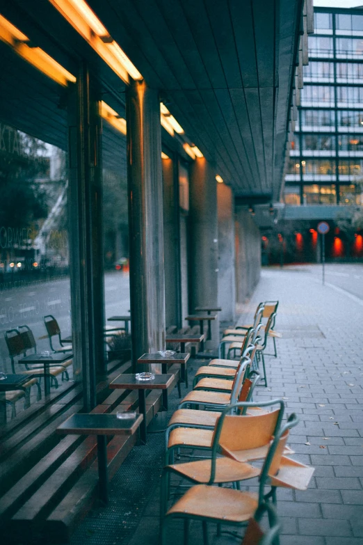 a row of chairs sitting in front of a building, by Niko Henrichon, unsplash, modernism, in a sidewalk cafe, early evening, square, wide film still