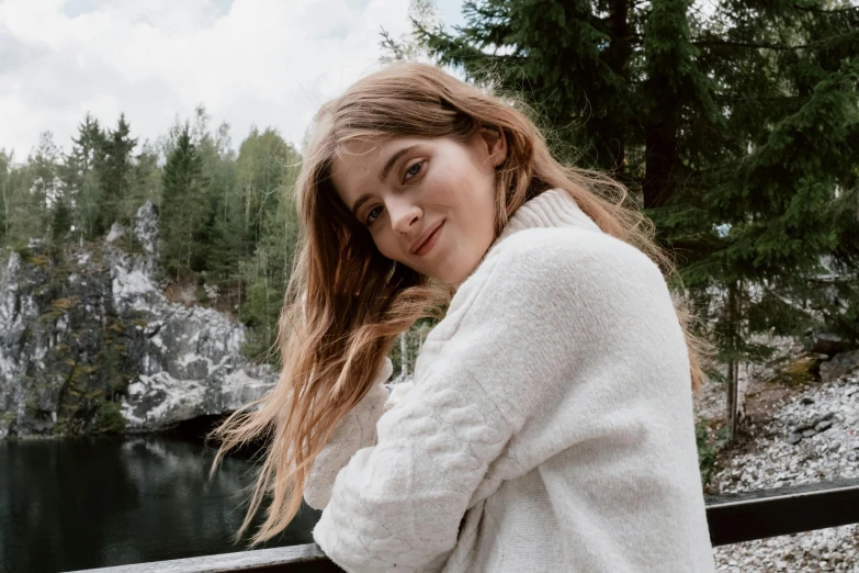 a woman standing on a bridge next to a body of water, inspired by Louisa Matthíasdóttir, trending on pexels, wearing a white sweater, portrait of barbara palvin, happy cozy feelings, in forest