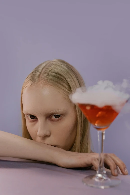 a woman sitting at a table with a drink in front of her, an album cover, inspired by Gottfried Helnwein, unsplash, surrealism, made of cotton candy, drinking a martini, eleven/millie bobbie brown, teenage girl