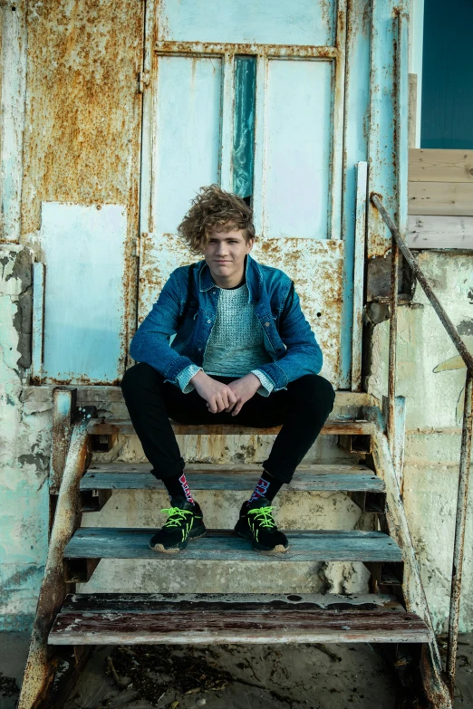 a man sitting on the steps of a run down building, an album cover, by Jacob Toorenvliet, trending on pexels, renaissance, he has short curly brown hair, confident pose, dale odell, sitting on a stool