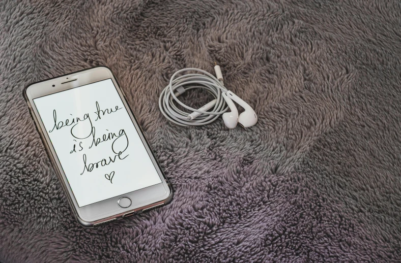 a cell phone sitting next to a pair of ear buds, an album cover, by Mardi Barrie, trending on pexels, happening, “modern calligraphy art, brave, cozy wallpaper, cables on floor