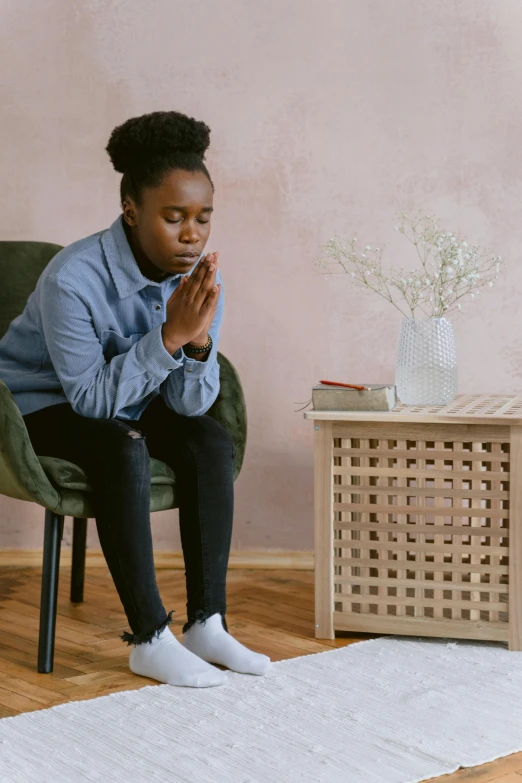 a woman sitting in a chair and praying, trending on unsplash, hurufiyya, black teenage boy, on a table, plain background, a person standing in front of a