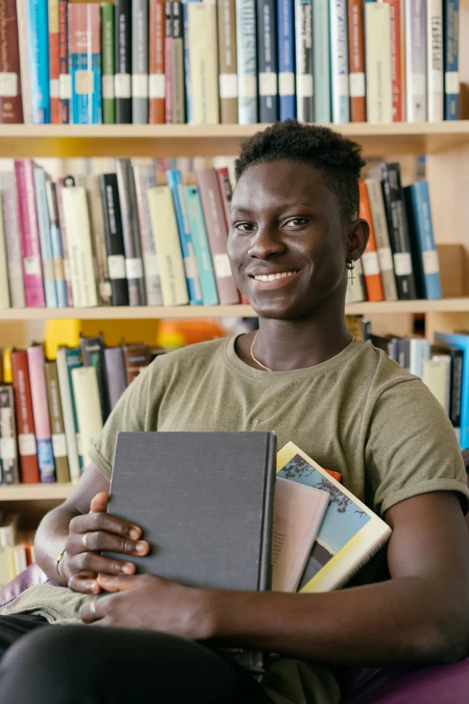 a man sitting in front of a bookshelf holding a book, brown skinned, college students, pastel', 2019 trending photo