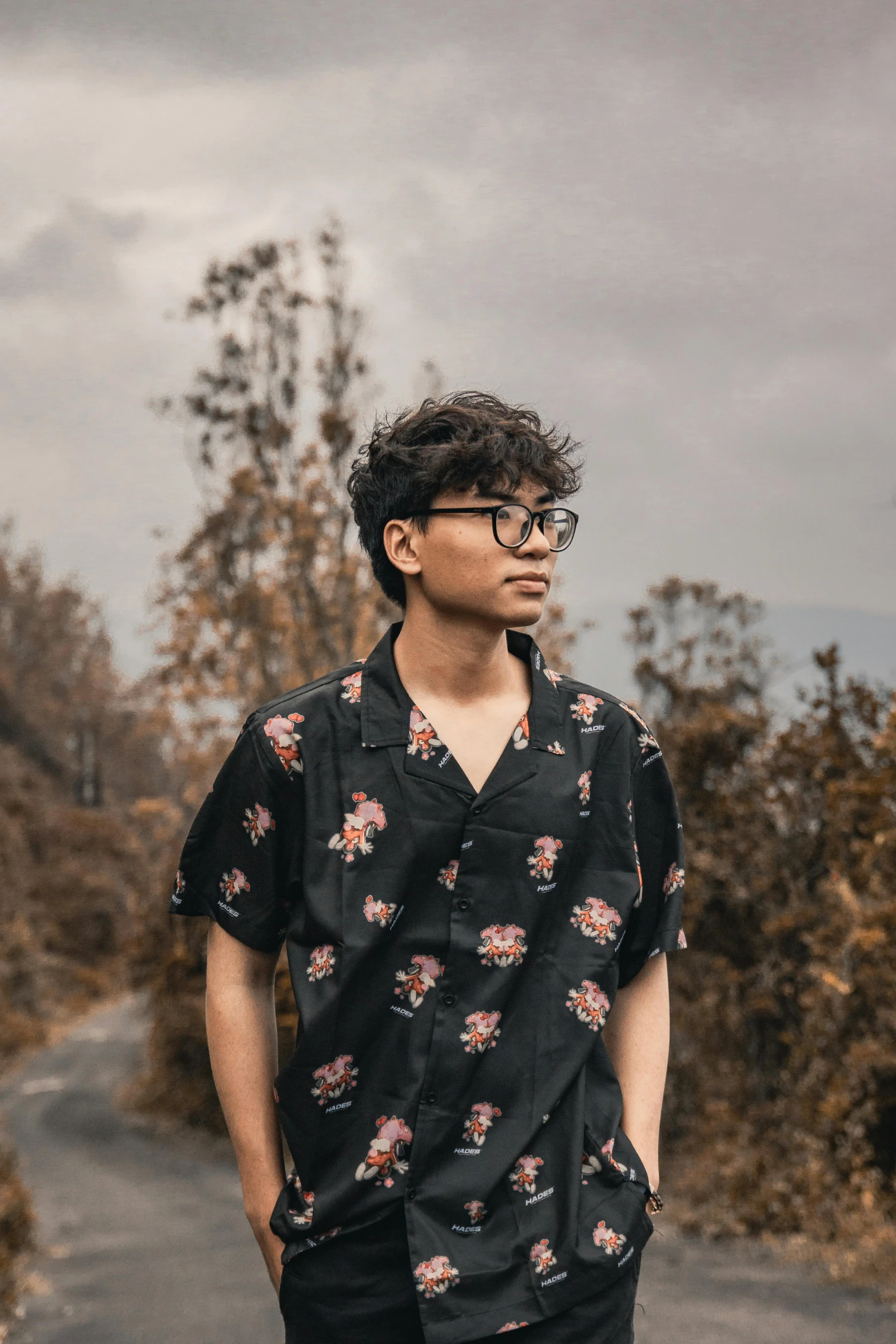 a man standing in the middle of a road, an album cover, inspired by Reuben Tam, pexels contest winner, sumatraism, floral clothes, wearing black glasses, profile image, androgynous male