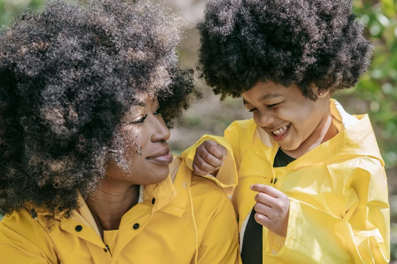 a woman standing next to a child in a yellow jacket, pexels, with afro, thumbnail, happy family, black