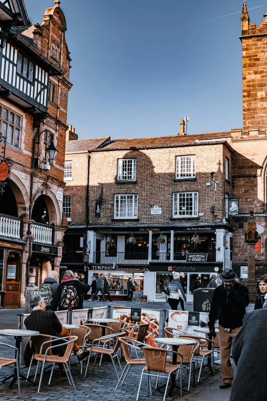 a group of people walking down a street next to tall buildings, renaissance, medieval tumbledown houses, chesterfield, people sitting at tables, wrought iron architecture