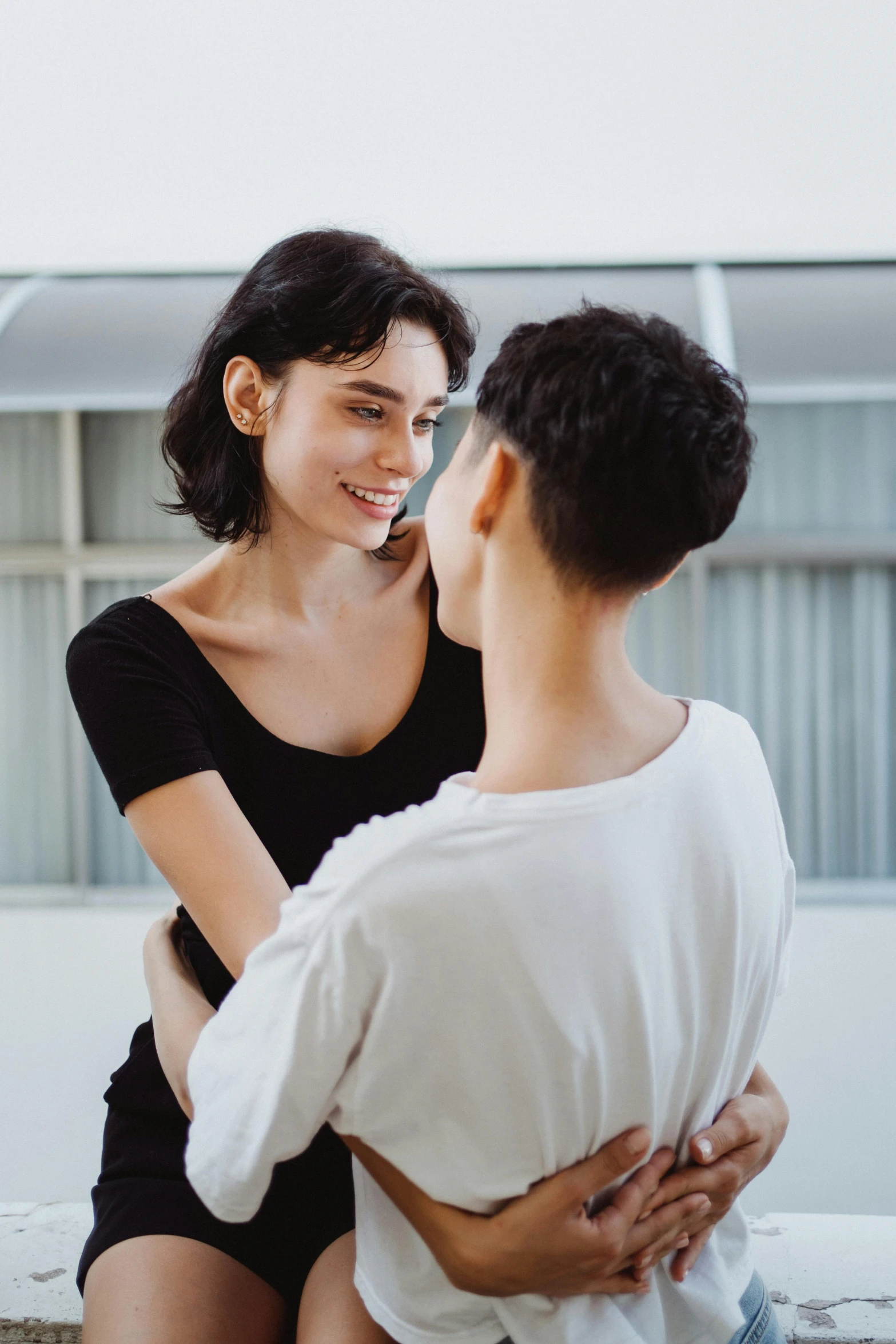 a woman sitting on top of a bed next to a man, trending on pexels, lesbian embrace, woman with black hair, looking at each other mindlessly, genderless