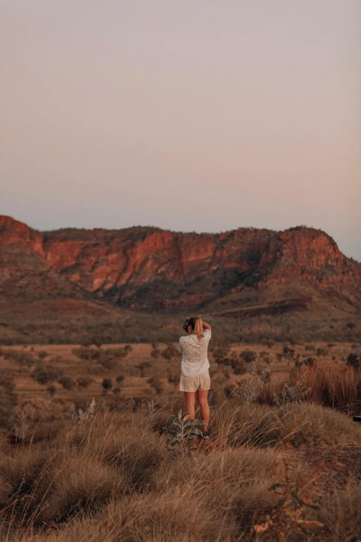 a woman standing on top of a grass covered field, by Lee Loughridge, unsplash contest winner, australian tonalism, desert in the background, 🤠 using a 🖥, in between a gorge, 3am