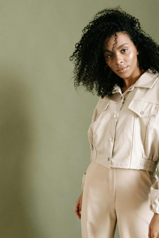 a woman standing in front of a green wall, an album cover, trending on pexels, renaissance, leather jacket and denim vest, beige cream natural muted tones, an all white human, thumbnail