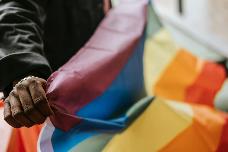 a close up of a person holding a rainbow flag, by Helen Stevenson, trending on unsplash, folds of fabric, brown, colorful signs, opening