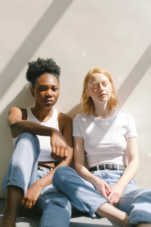 a couple of women sitting next to each other, by Gee Vaucher, trending on unsplash, renaissance, dressed in a white t-shirt, fair complexion, black young woman, jeans and t shirt