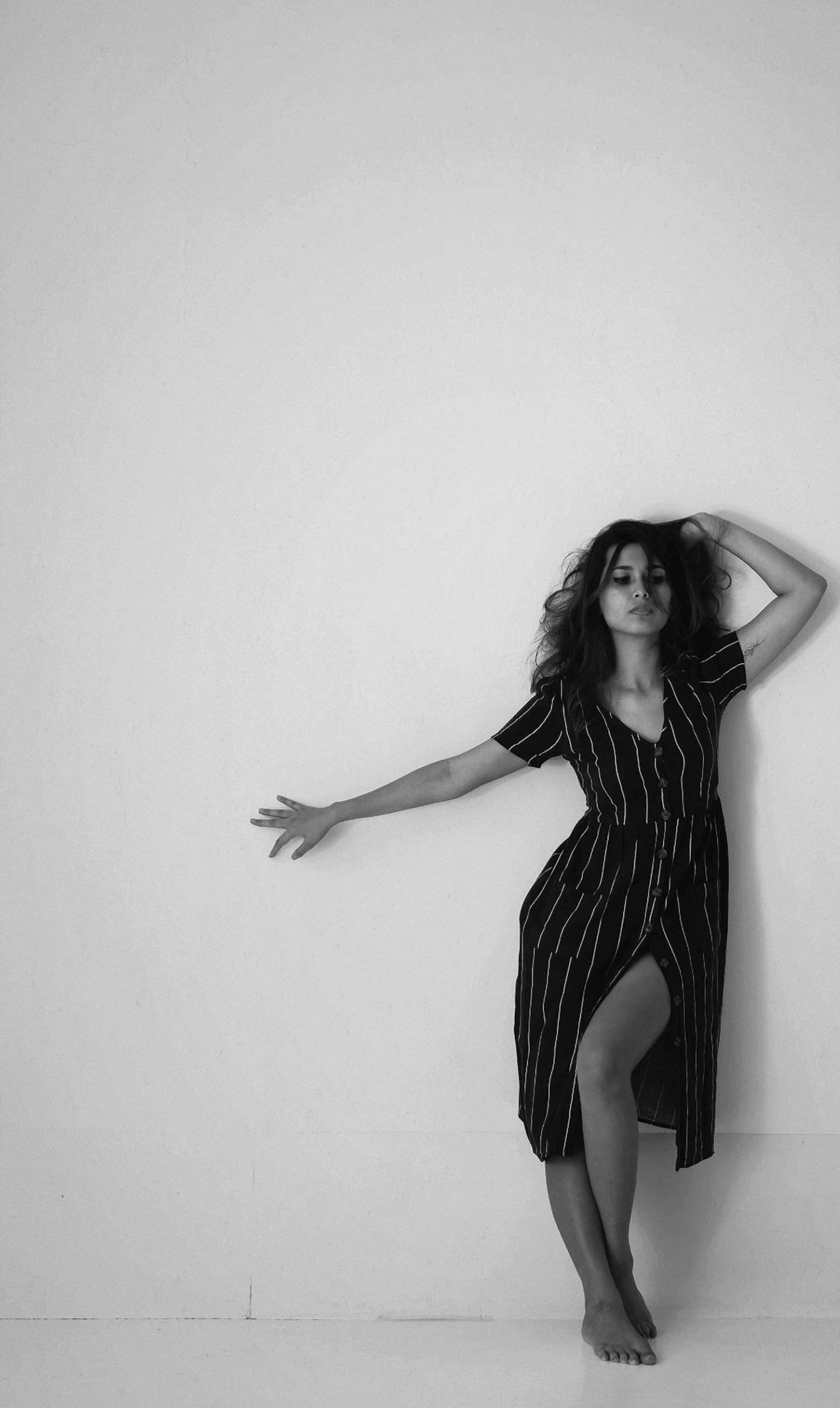 a black and white photo of a woman leaning against a wall, unsplash, conceptual art, charli xcx, arms stretched out, imaan hammam, girl in a dress