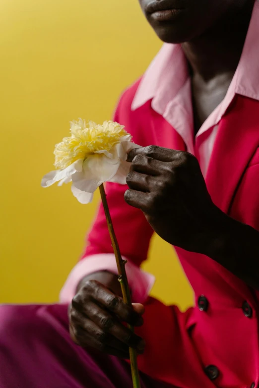 a man sitting down with a flower in his hand, by Nathalie Rattner, adut akech, raspberry banana color, ignant, zoomed in