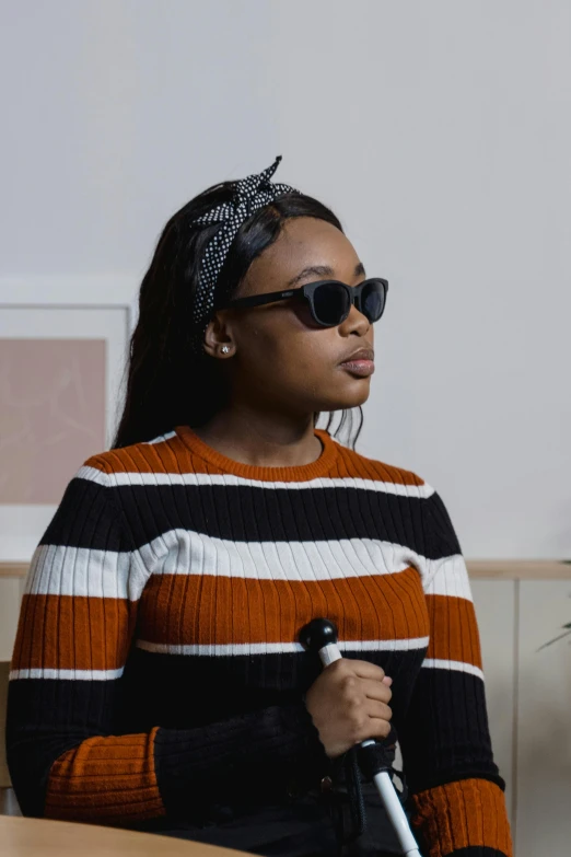 a woman sitting at a table with a cane, trending on pexels, wearing shades, black teenage girl, wearing a sweater, wearing stripe shirt
