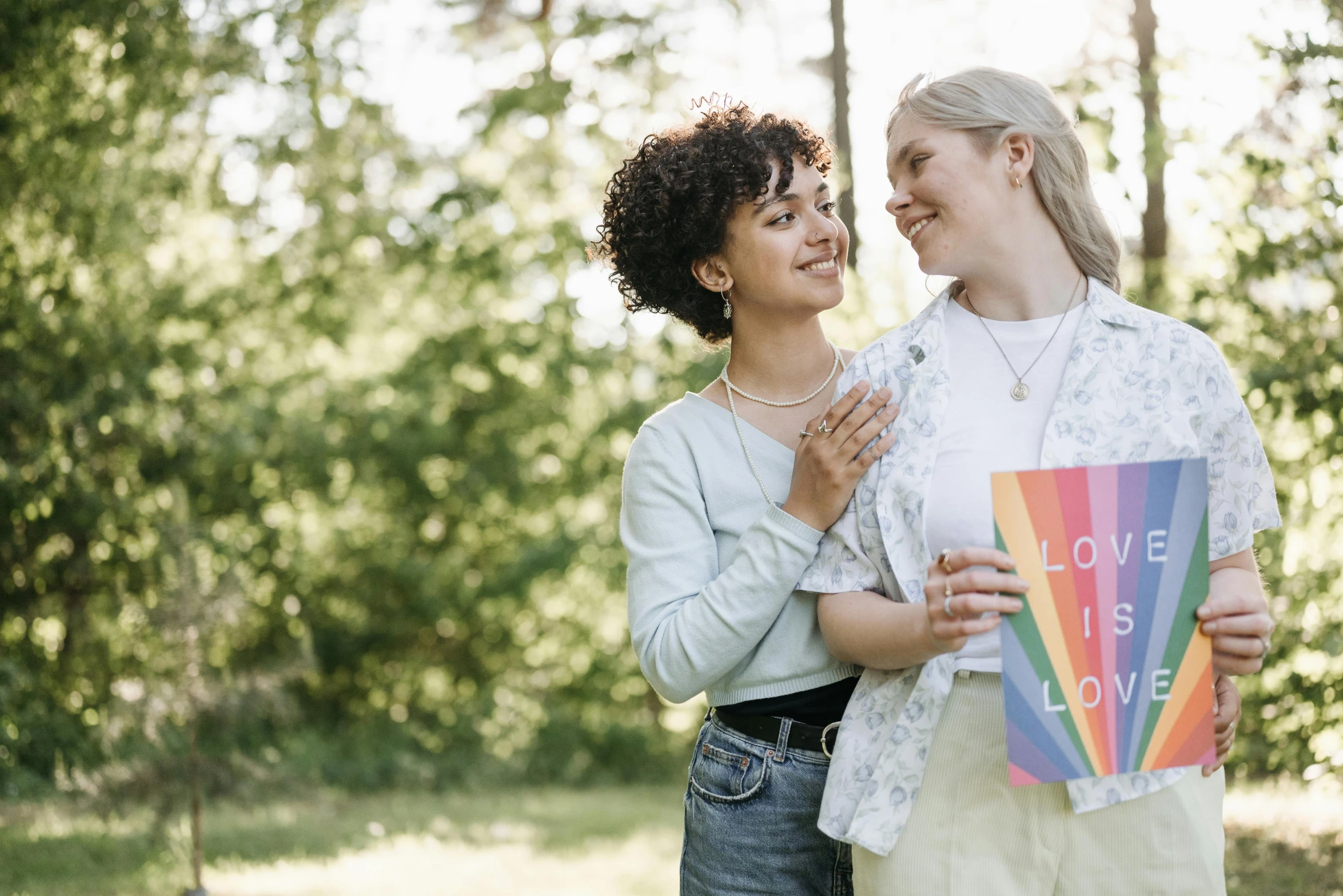 a couple of women standing next to each other, pexels, happening, pride month, holding a book, love os begin of all, outdoor photo