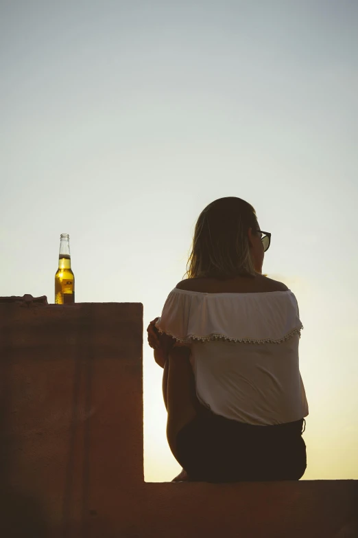 a woman sitting on a ledge next to a bottle of beer, pexels contest winner, standing alone, gold hour, rooftop romantic, but minimalist