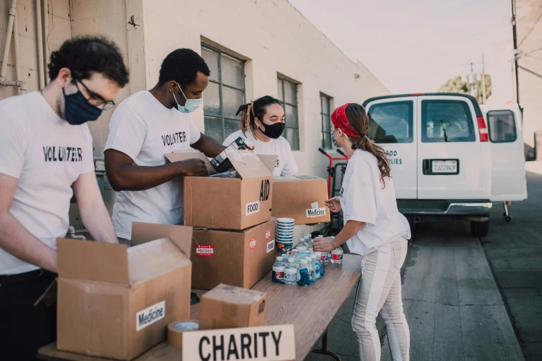 a group of people standing around a table filled with boxes, by Francis Helps, pexels contest winner, hunger, people are wearing masks, background image, los angeles