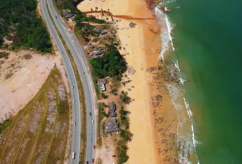 an aerial view of a beach next to the ocean, by Luis Miranda, pexels contest winner, photorealism, damaged streets, red sand, deforestation, highway