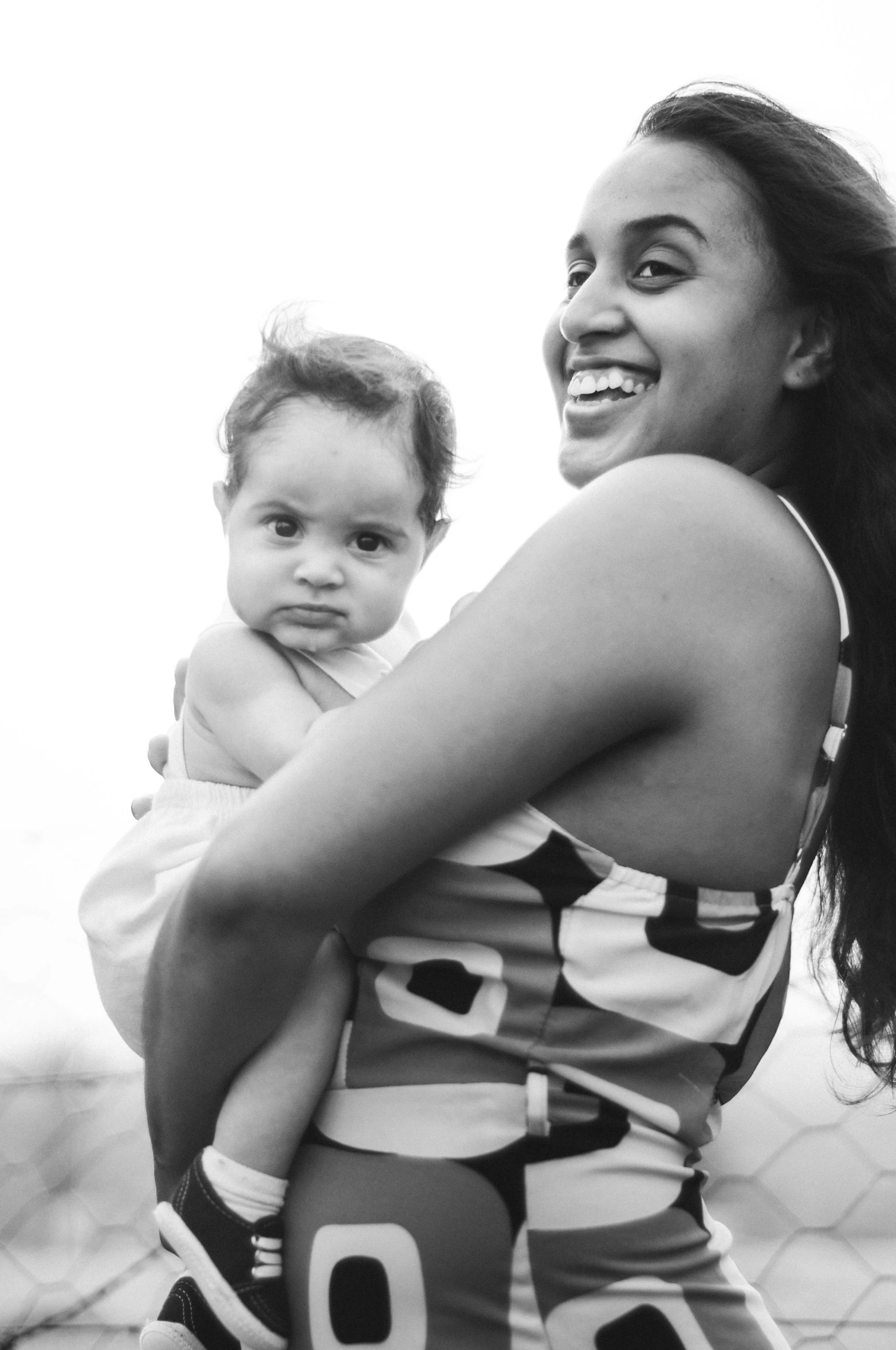 a black and white photo of a woman holding a baby, a black and white photo, by Lily Delissa Joseph, smiling confidently, moana, square, beach